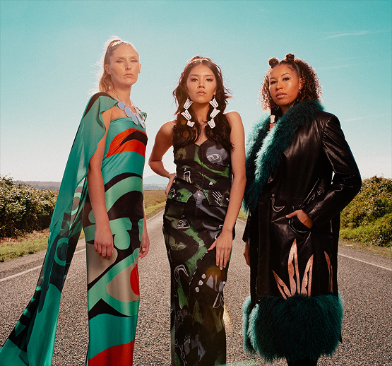 Three Indigenous women model stylish dresses and jackets.