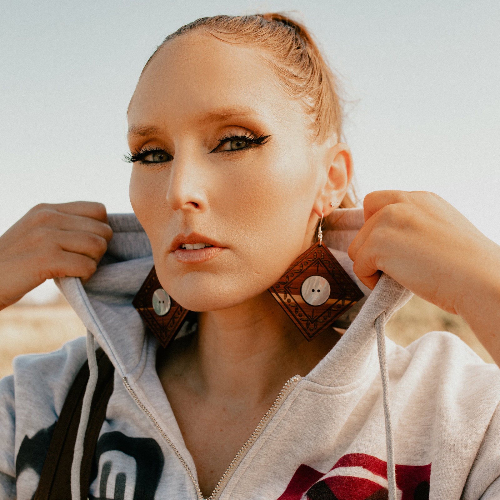 Model looks at camera while wearing a pair of "Ancestral Framing" earrings from Copper Canoe Woman.