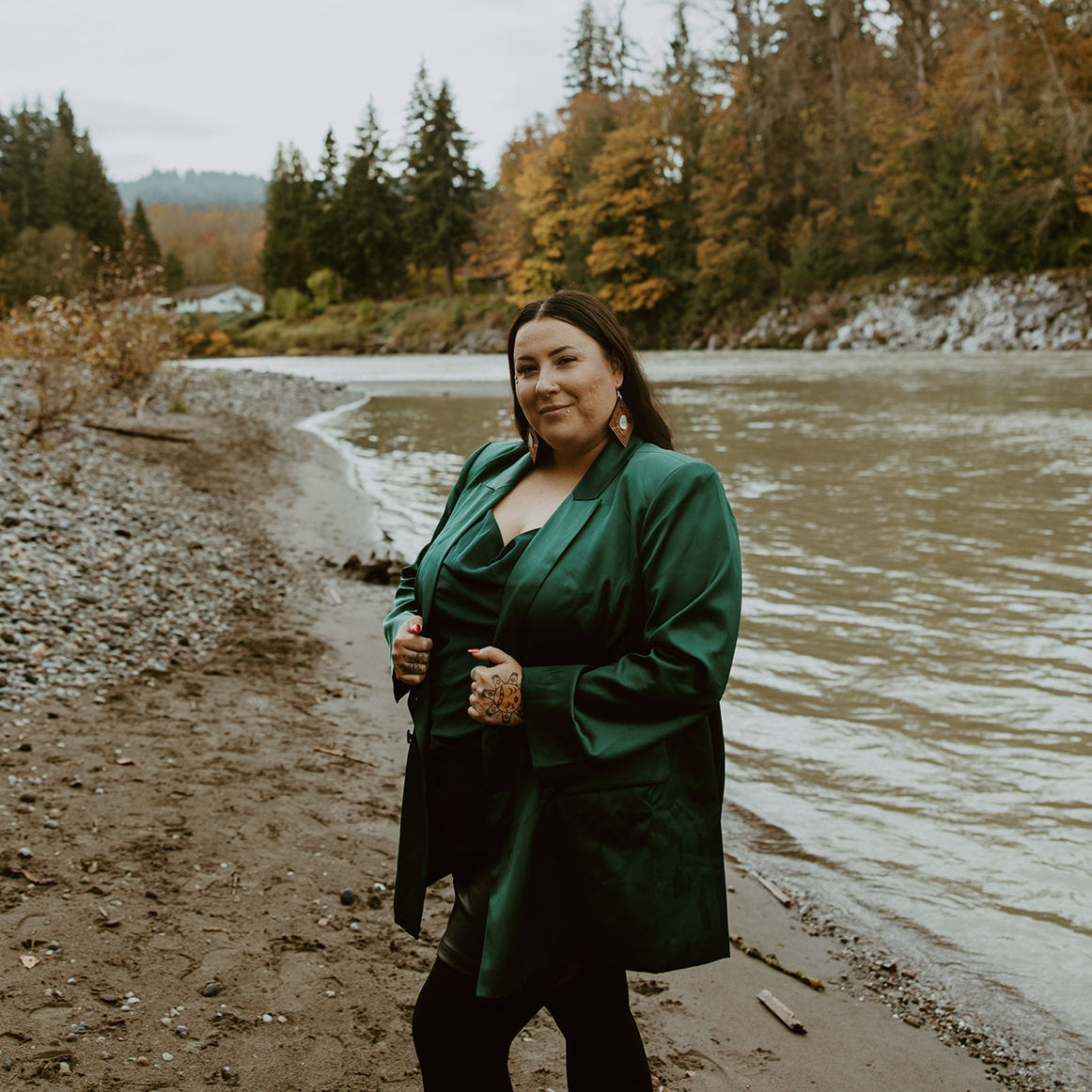 A model stands near a river wearing a pair of cedar wood "Ancestral Framing" earrings from Copper Canoe Woman.