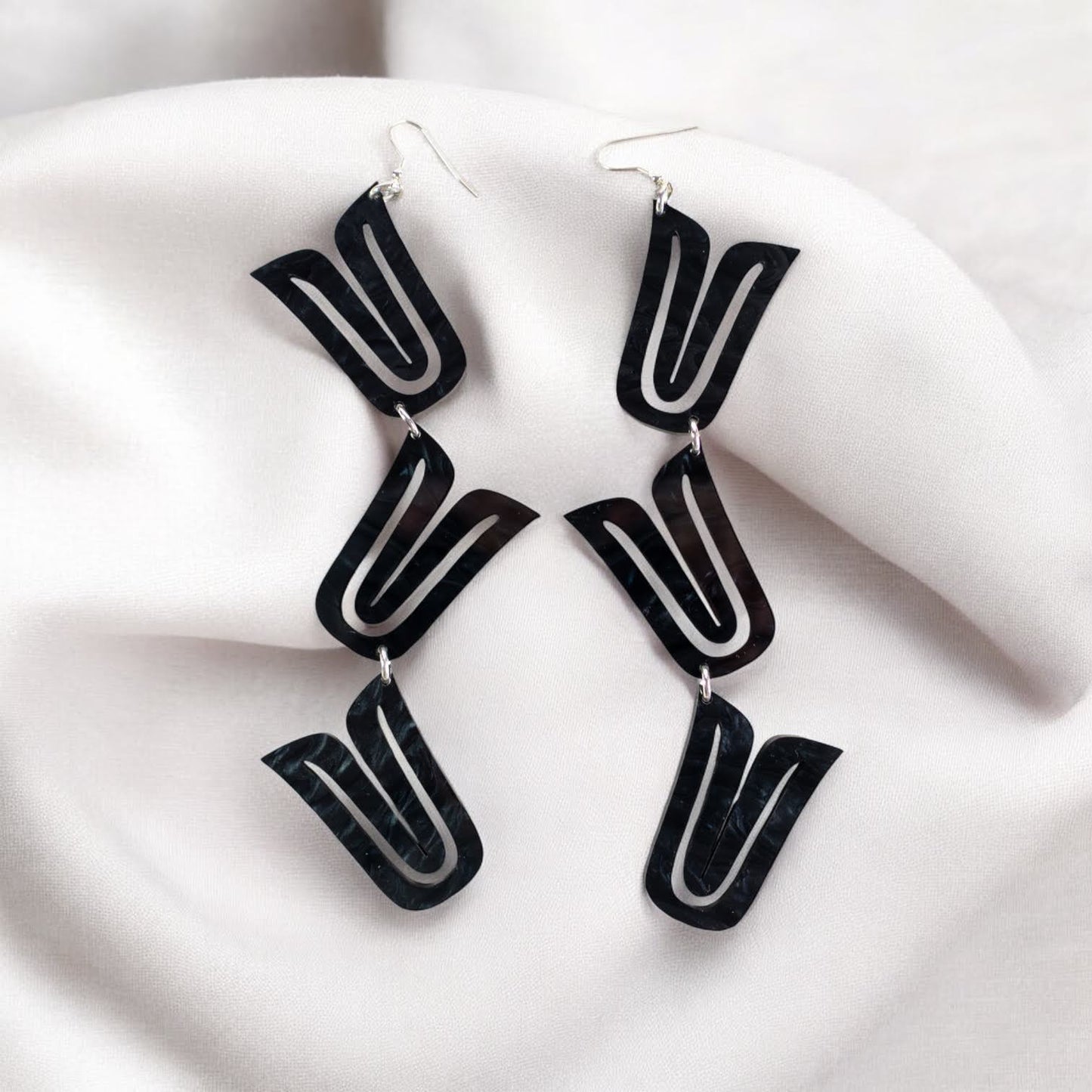 A pair of black "Formline Cascade" earrings from Copper Canoe Woman laying in white fabric.