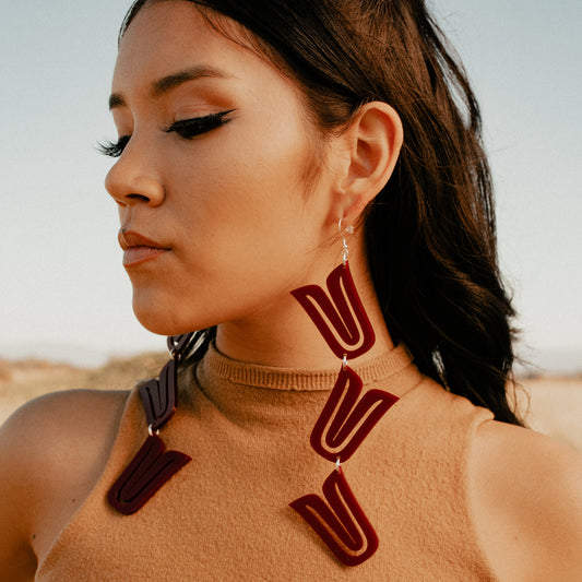 A model stands in a field wearing red acrylic "Formline Cascade" earrings from Copper Canoe Woman.