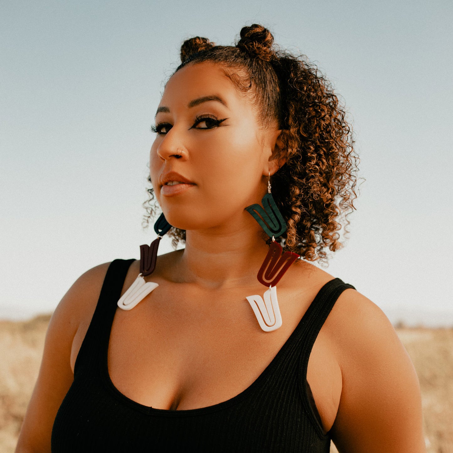 A model stands in a field wearing a pair of mixed acrylic "Formline Cascade" earrings by Copper Canoe Woman.