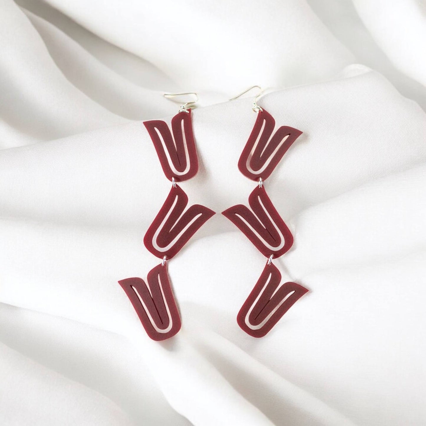 A pair of red acrylic "Formline Cascade" earrings from Copper Canoe Woman rest on white fabric.