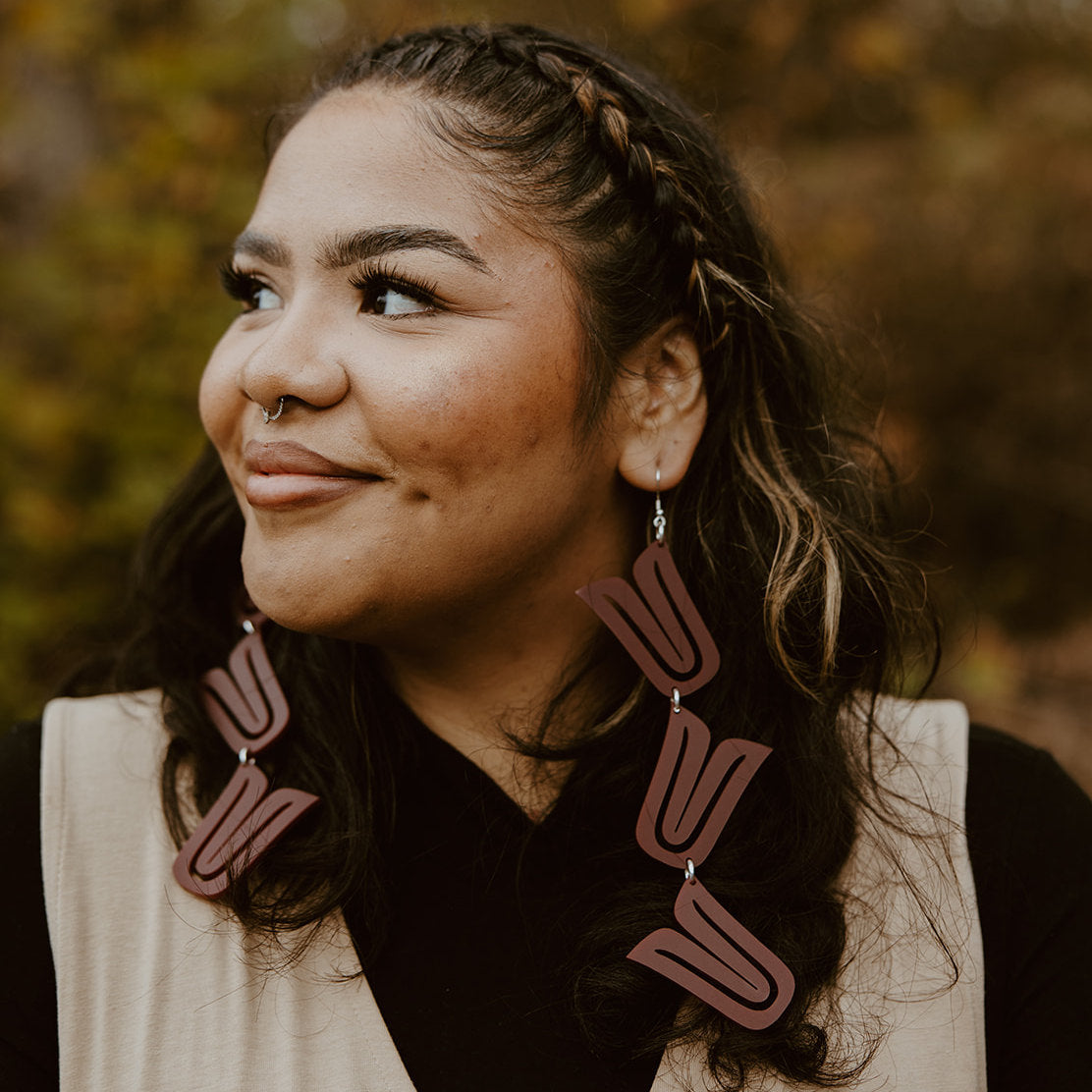 A model wearing the red acrylic style of the "Formline Cascade" earring by Copper Canoe Woman.