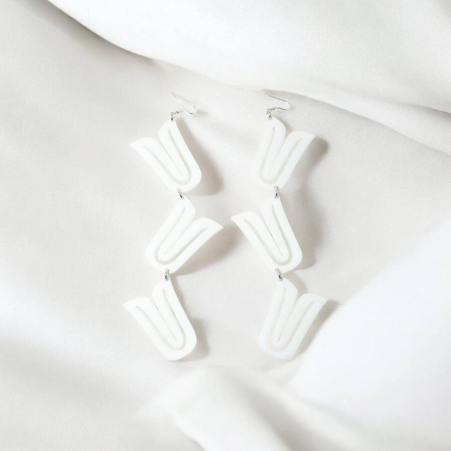The "Formline Cascade" earring in white from Copper Canoe Woman laying on white fabric.