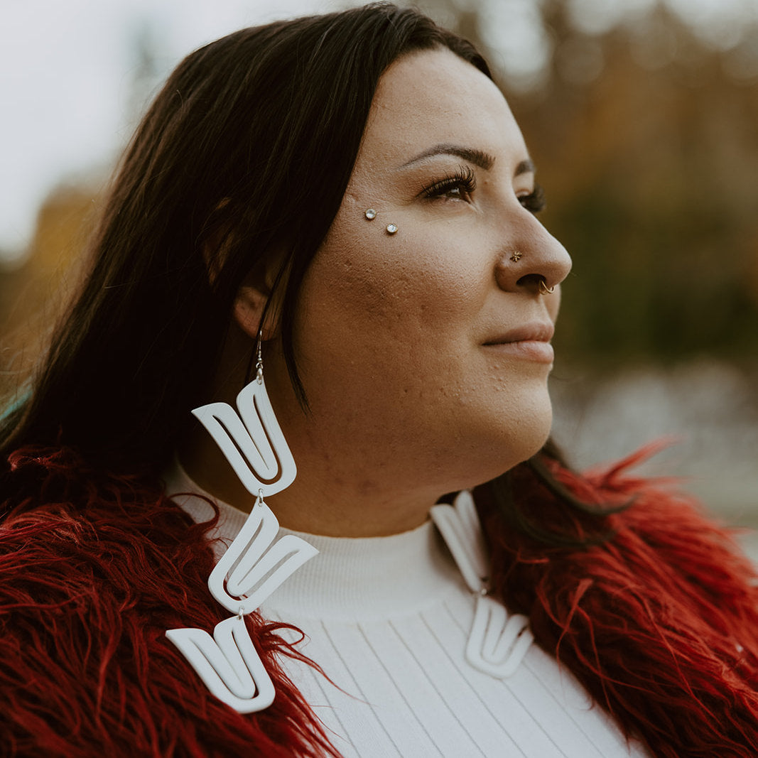 A model in profile wearing white acrylic "Formline Cascade" earrings from Copper Canoe Woman.