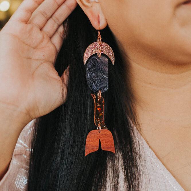 close up of woman wearing abstract formline art earring in color sequence of rose gold glitter, galaxy purple, copper glitter, and wood from copper canoe woman.