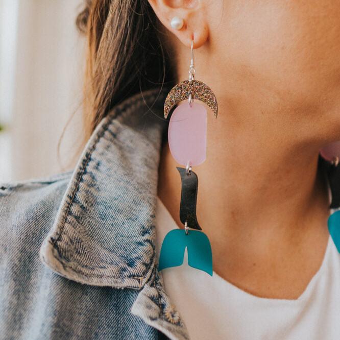 close up of woman wearing abstract formline art earring in color sequence of multi color glitter, lavender, galaxy purple, frosted blue from copper canoe woman.