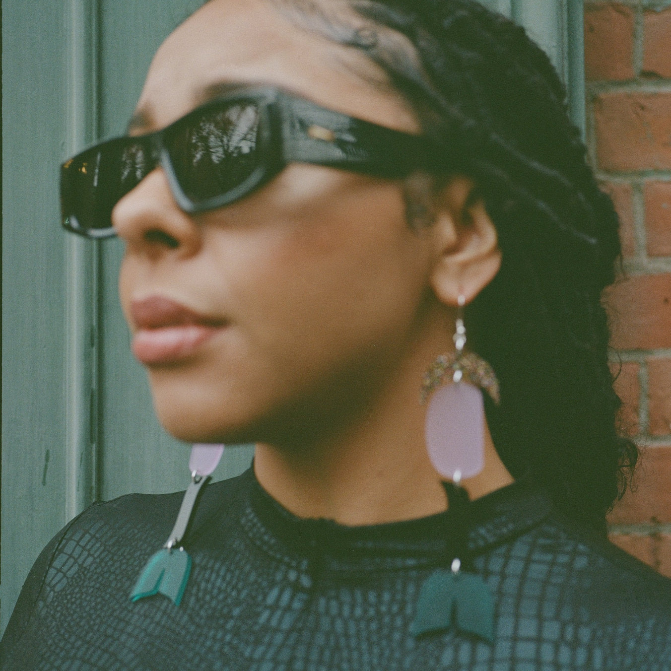 woman wearing abstract formline art earring in color sequence of multi color glitter, lavender, galaxy purple, teal from copper canoe woman.