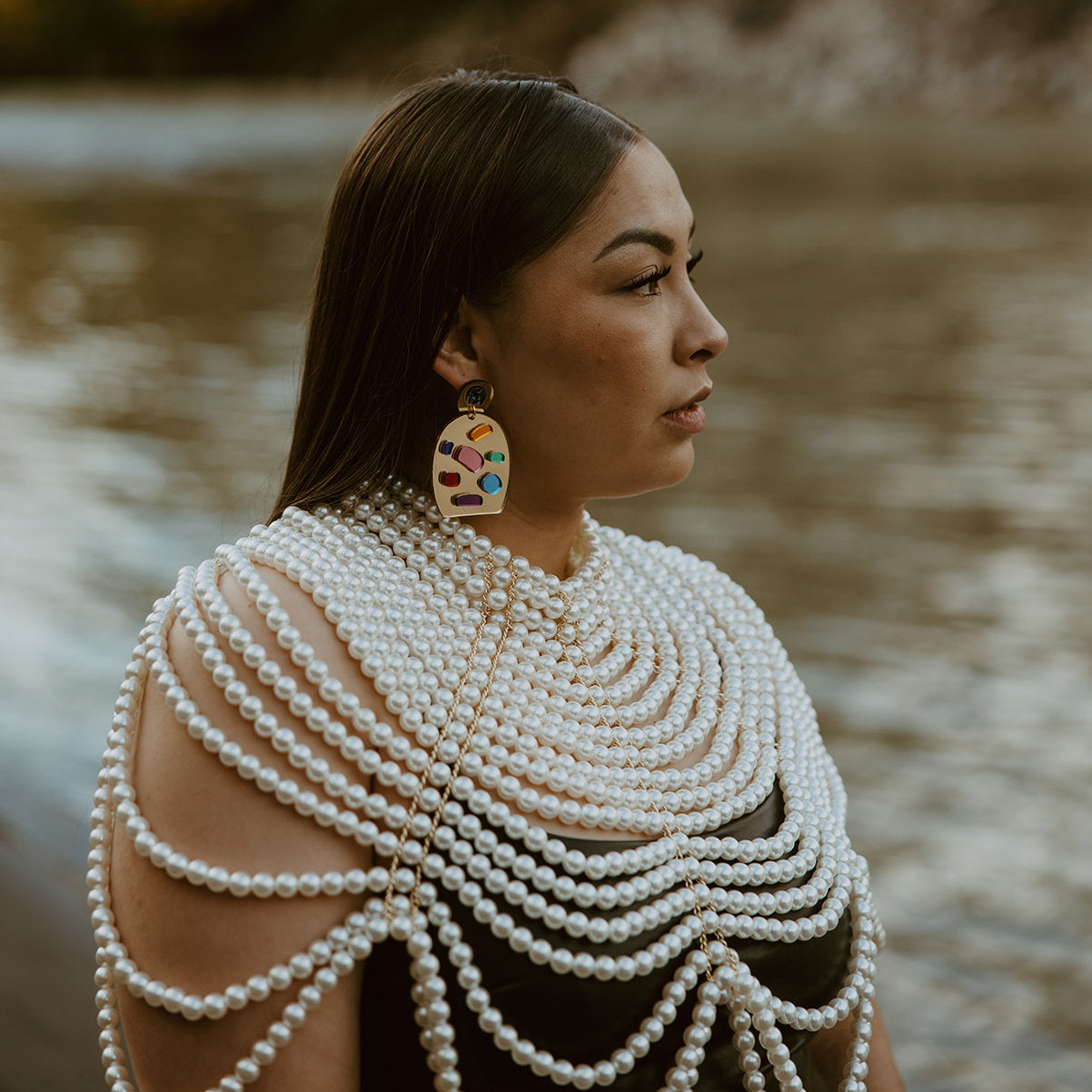 A model stands by water wearing the post style of the ovoid-shaped version of the "Generational Love" earring from Copper Canoe Woman.