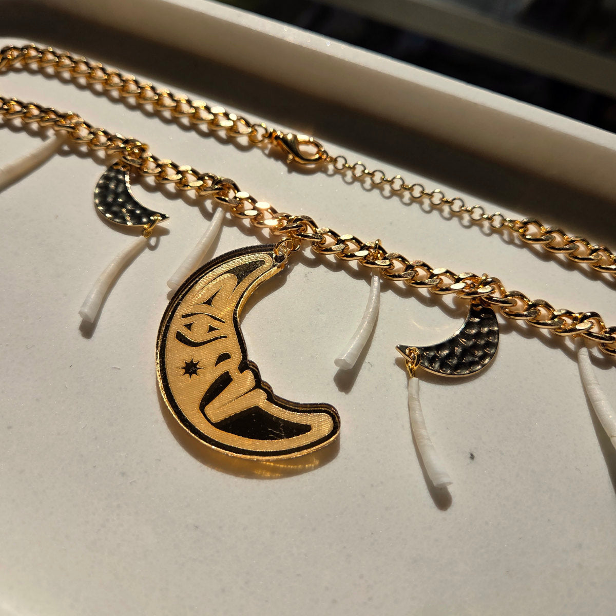 Gold chain necklace with moon pendant and dentalium on a white surface from Copper Canoe Woman.