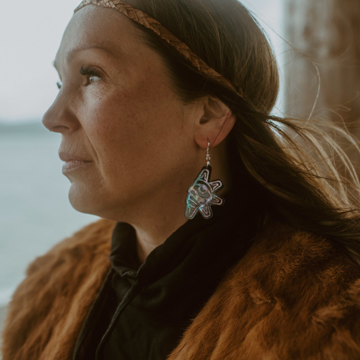 A model stares at the ocean wearing "Hupal" sun and moon earrings from Copper Canoe Woman.