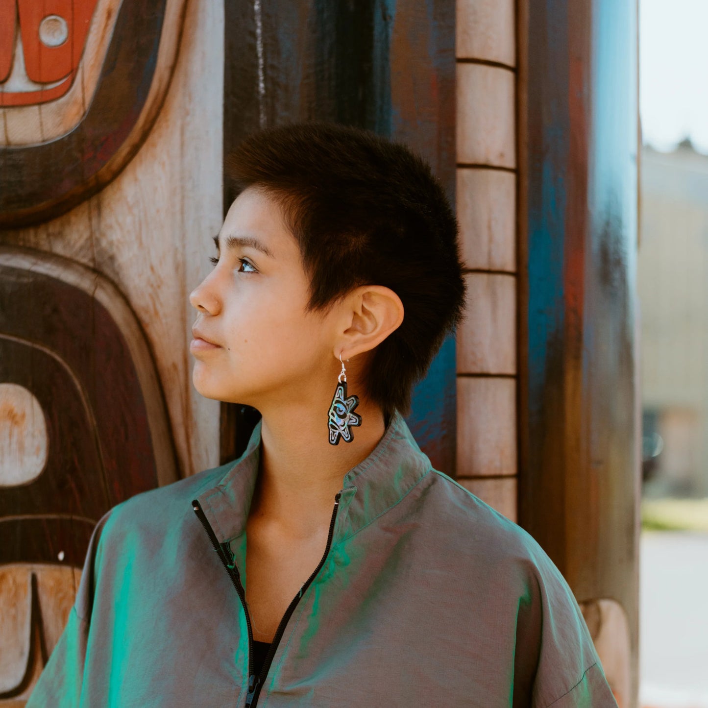A youth model stares into the distance wearing the "Hupal" sun and moon earrings from Copper Canoe Woman.