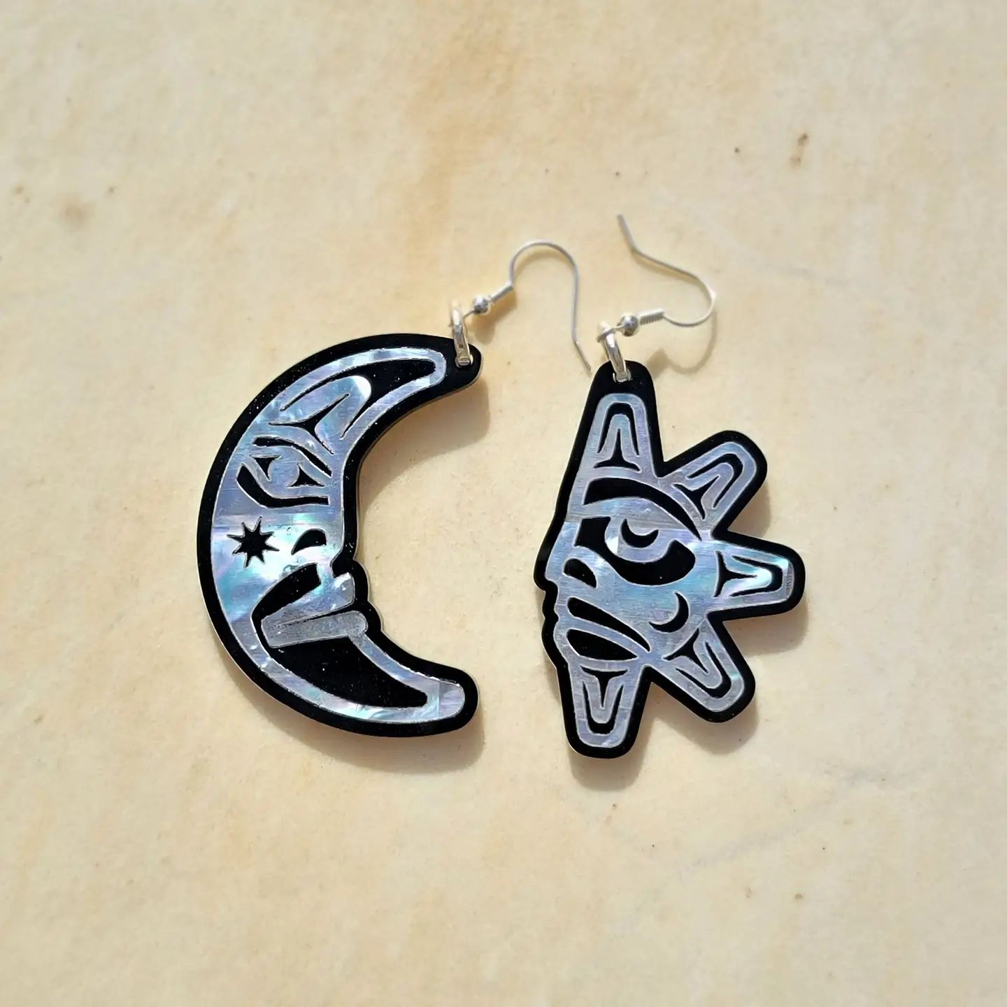 A pair of Copper Canoe Woman "Hupal" sun and moon earrings lay on a table.