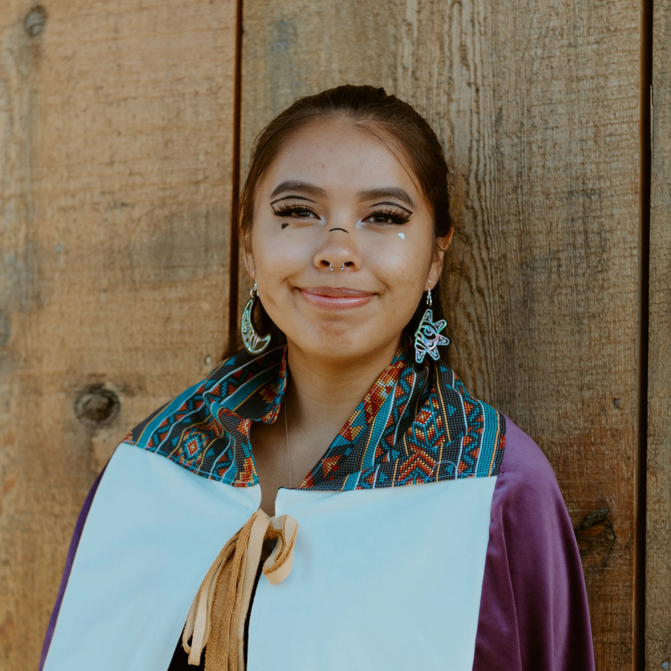 A youth in Indigenous regalia wears a pair of "Hupal" sun and moon earrings from Copper Canoe Woman.