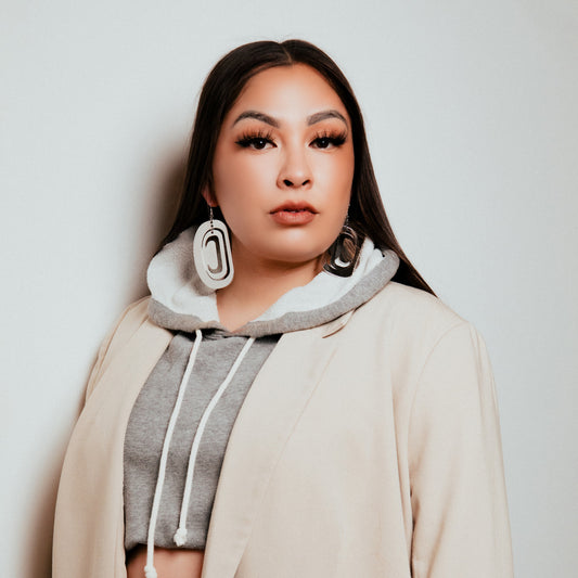 A person wearing rhodium platinum large ovoid earrings from Copper Canoe Woman with a grey hoodie and a beige coat.