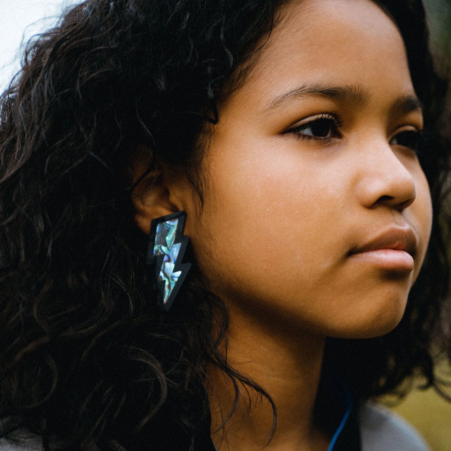 A youth model wearing black acrylic lighting bolt earrings with abalone inlay from Copper Canoe Woman.