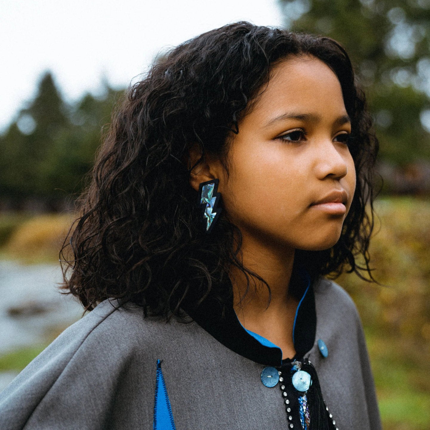 Copper Canoe Woman lightning bolt earrings in black acrylic with abalone inlay worn by a youth model.