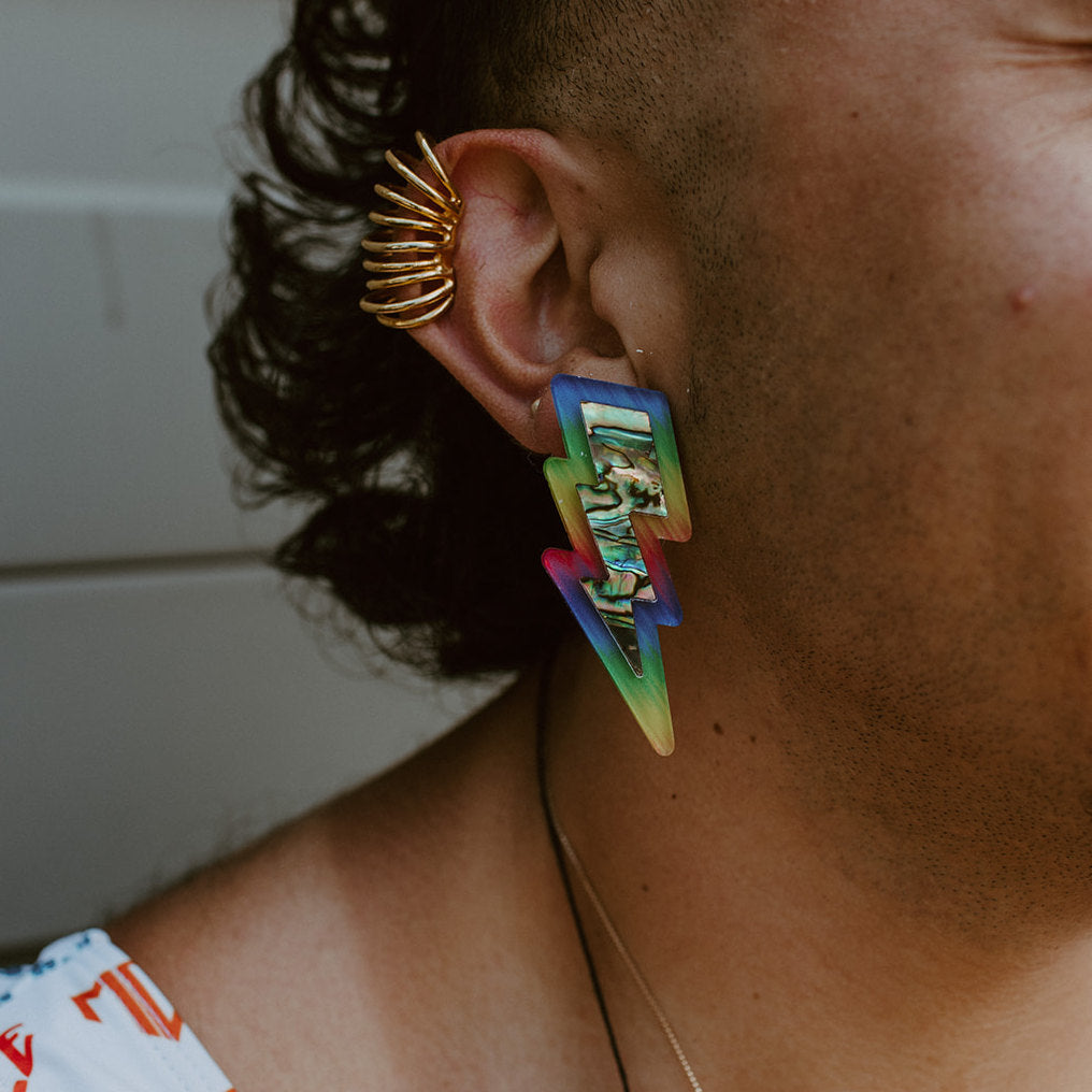 A close up of a model wearing the pride rainbow acrylic lightning bolt earrings from Copper Canoe Woman.