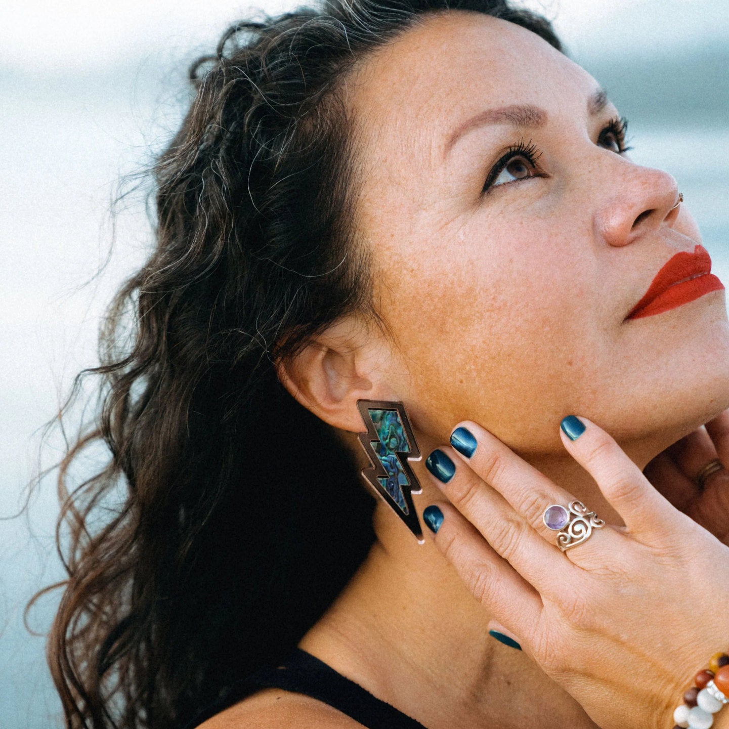 Model stare up at the sky while wearing lightning bolt earrings with abalone shell inlay in a rose gold mirror acrylic from Copper Canoe Woman.