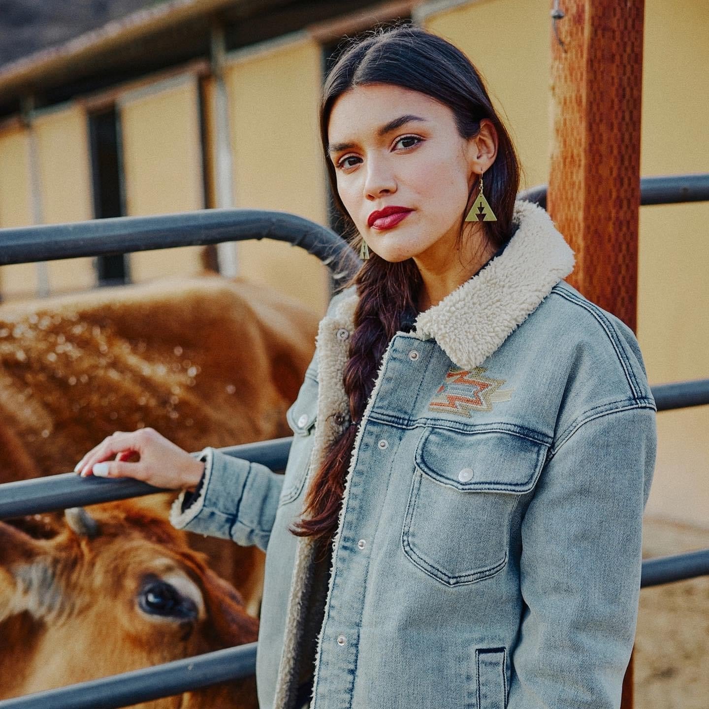 Woman standing at a fence wearing brass triangle earrings with southwest geometric shapes from Copper Canoe Woman.