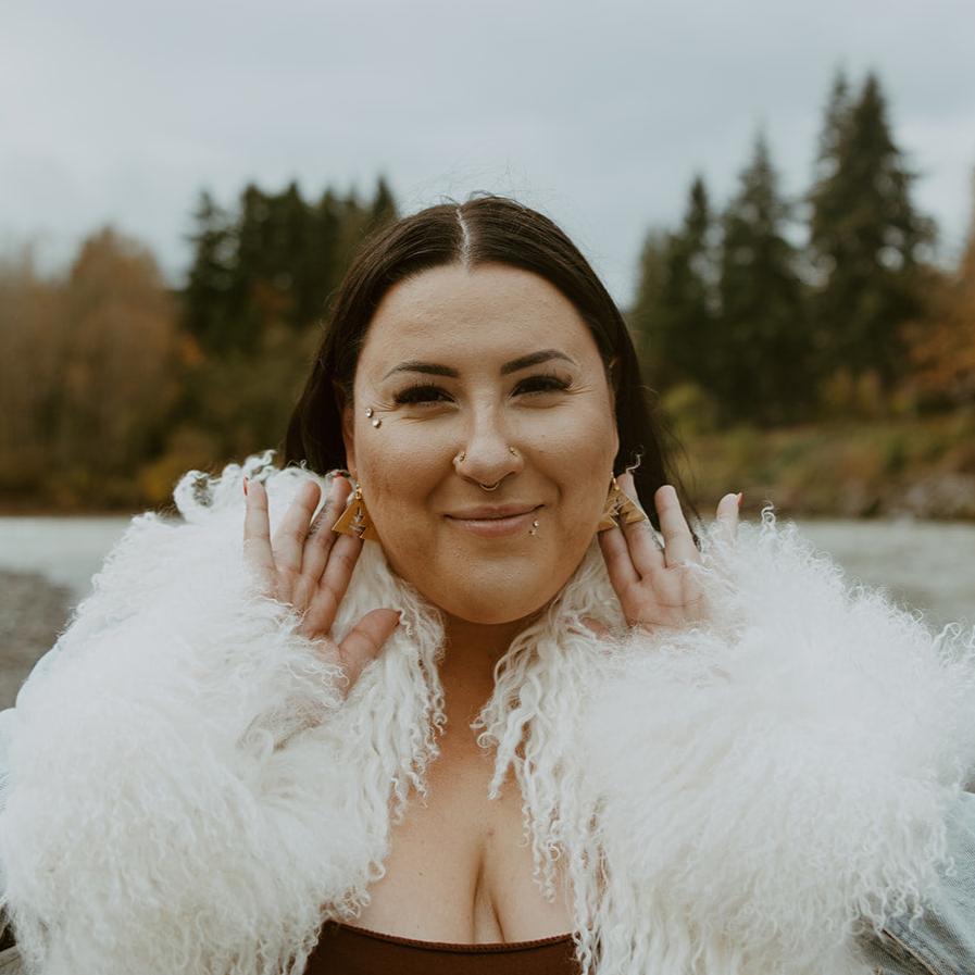 Woman stares at camera and shows off brass triangle earrings with southwest geometric shapes from Copper Canoe Woman.