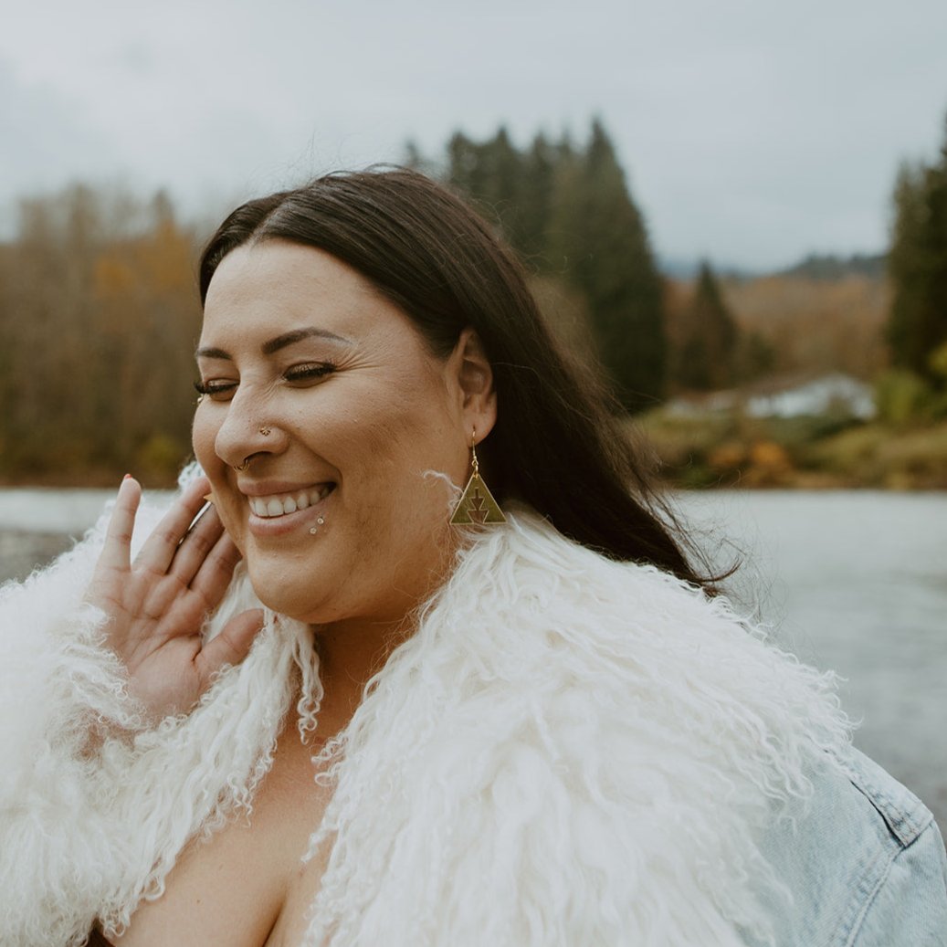 Woman smiling while wearing brass triangle earrings with southwest geometric shapes from Copper Canoe Woman.