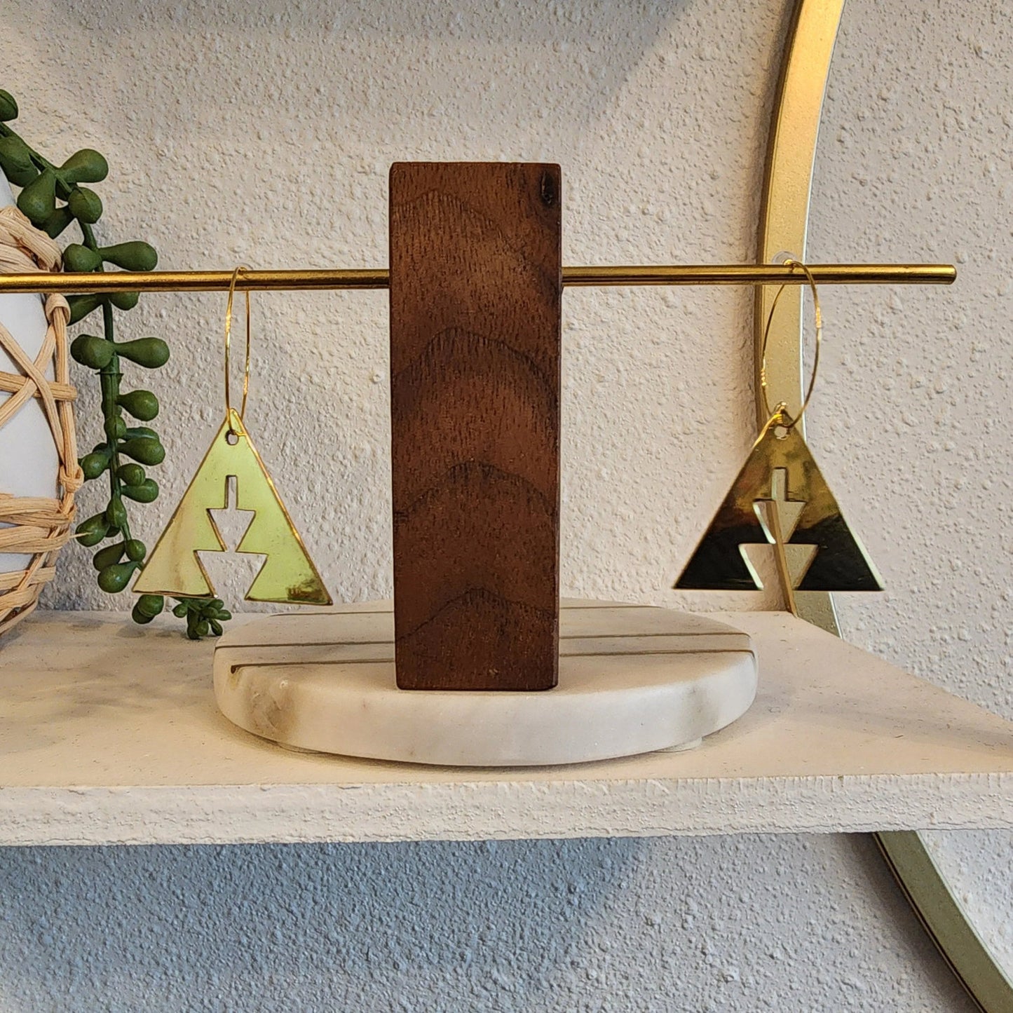 A pair of brass triangle earrings with southwest geometric shapes from Copper Canoe Woman resting on a jewelry display.