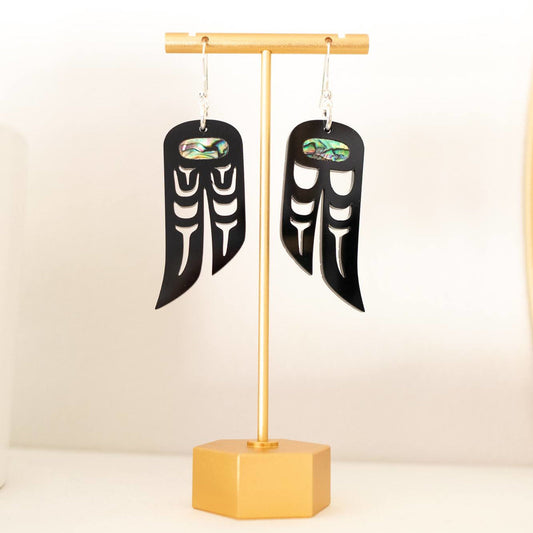 A pair of "Love Birds" earrings in black acrylic from Copper Canoe Woman hand from an earring stand.