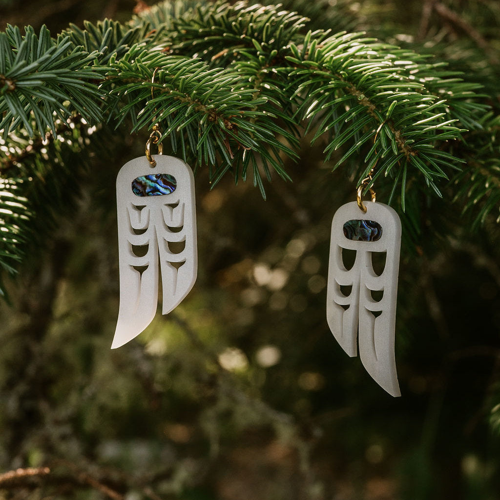 Copper Canoe Woman "Love Birds" earrings in pearlescent acrylic hang from a pine branch.