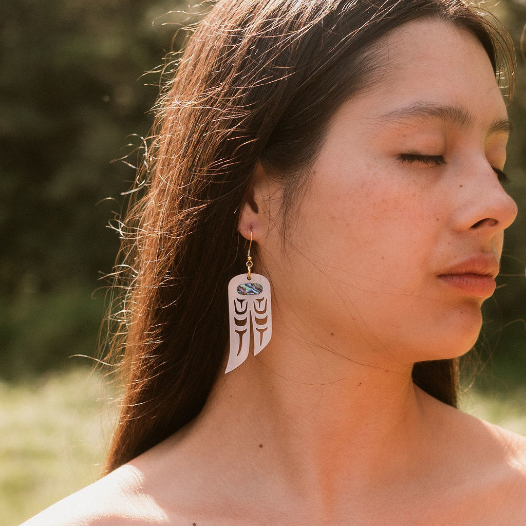 A model wears a pair of "Love Birds" earrings in pearlescent acrylic from Copper Canoe Woman.