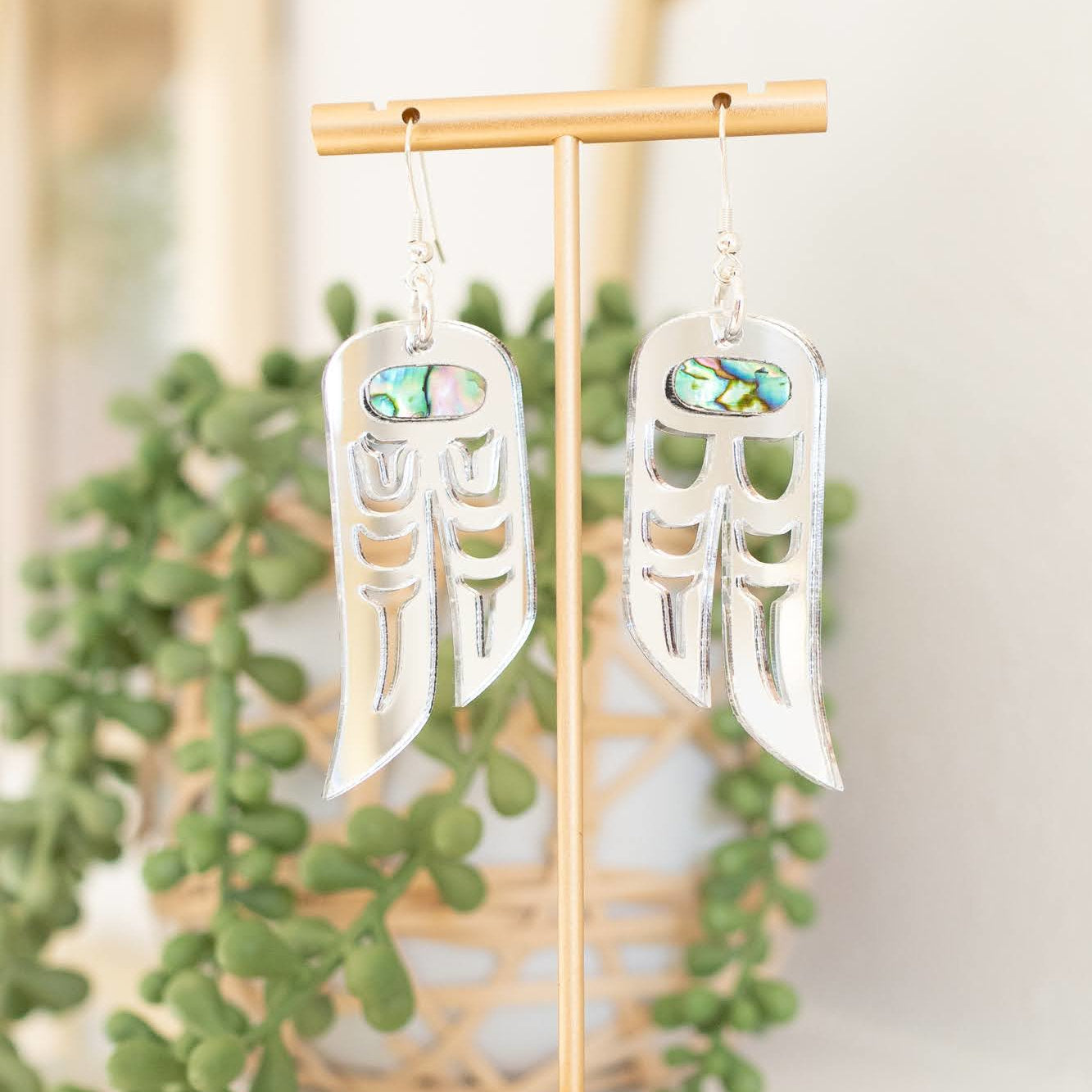 A pair of silver mirror acrylic "Love Birds" earrings from Copper Canoe Woman hang from a display stand.
