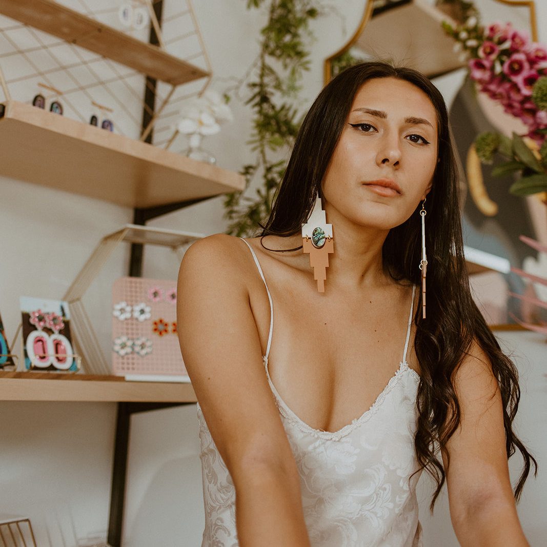 A model wears the "Mesa" earrings from Copper Canoe Woman in cream and terracotta acrylic.