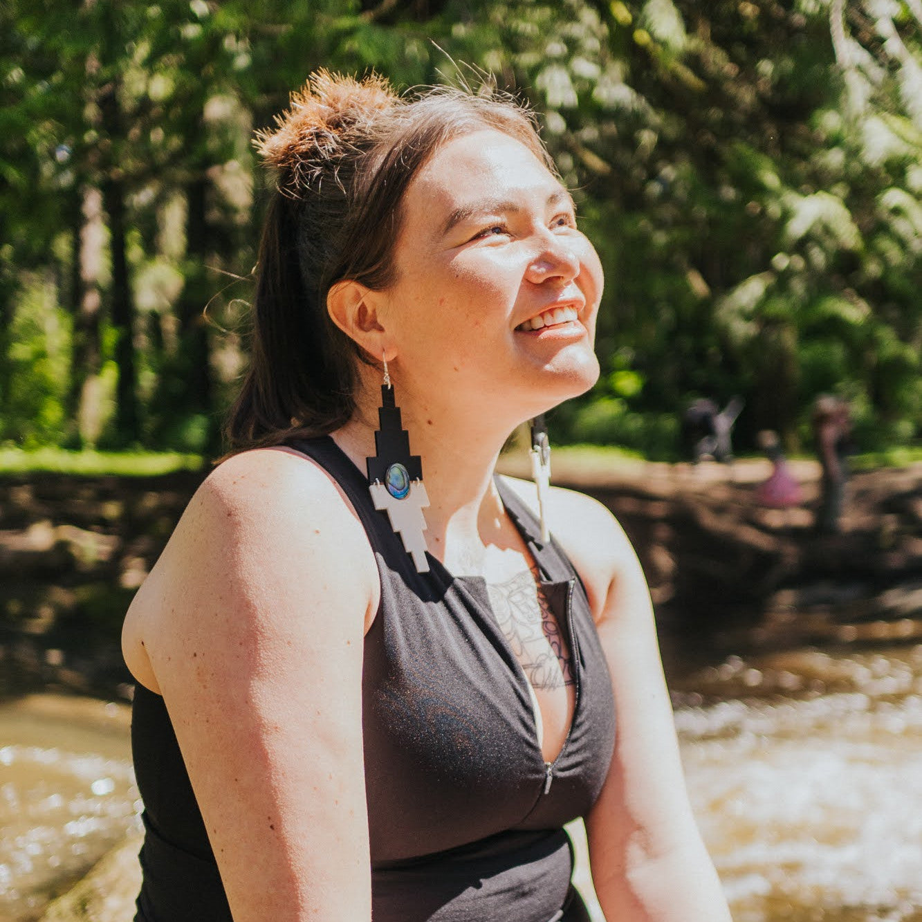 A model smiles in the sun wearing jet black and cream acrylic "Mesa" earrings from Copper Canoe Woman.