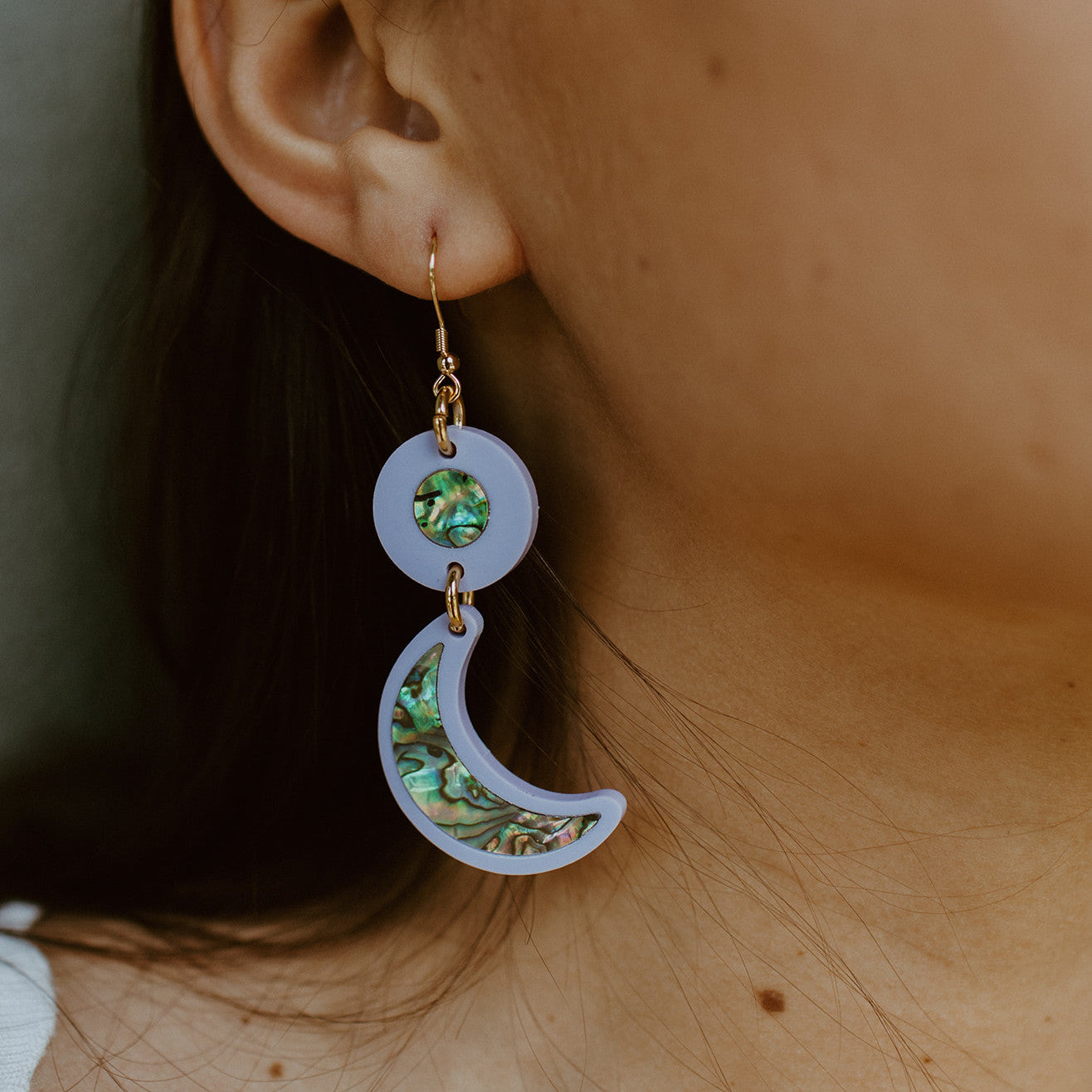 Closeup of a model wearing the lavender acrylic hook "Nuci" crescent moon earrings from Copper Canoe Woman.