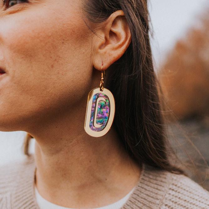 Closeup of a model on a beach wearing "Abalone Ovoid" earrings in gold mirror acrylic.