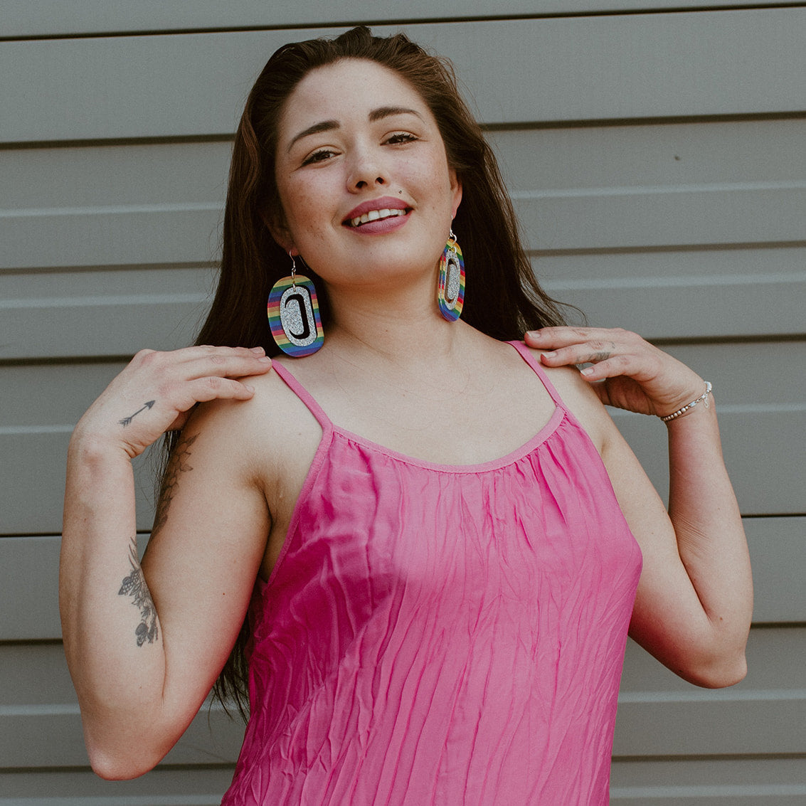 A model wears a pair of rainbow and holographic glitter acrylic large ovoid earrings from Copper Canoe Woman.