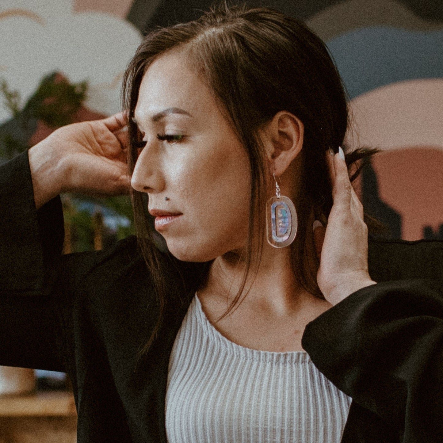 A model wearing a pair of "Abalone Ovoid" earrings in rose gold mirror acrylic from Copper Canoe Woman.