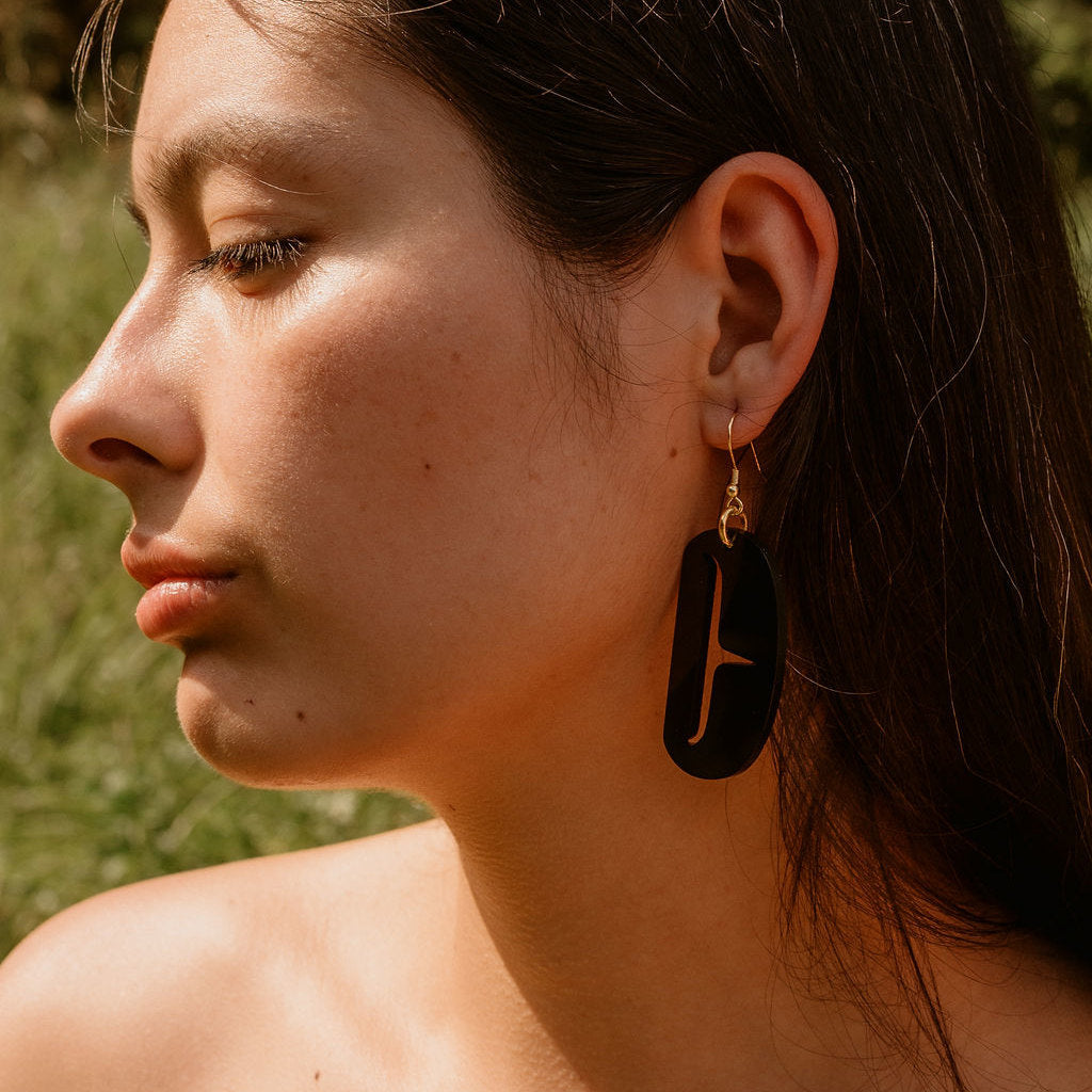 Close-up of a woman wearing black earrings with a blurred natural background