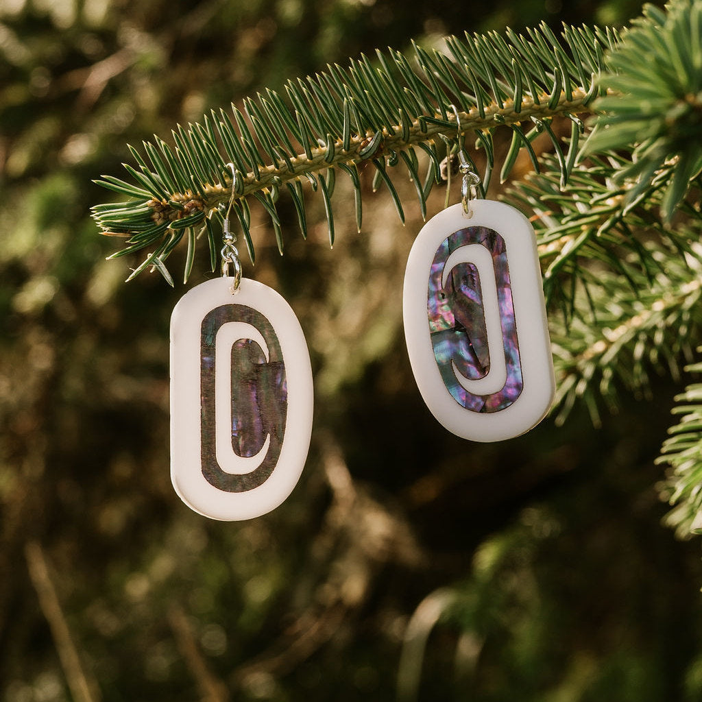 White acrylic Abalone Ovoid earrings from Copper Canoe Woman hanging from a branch.