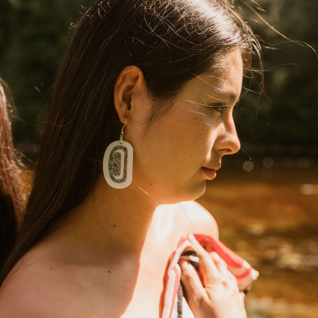A woman in profile wears "Abalone Ovoid" earrings in white acrylic from Copper Canoe Woman.