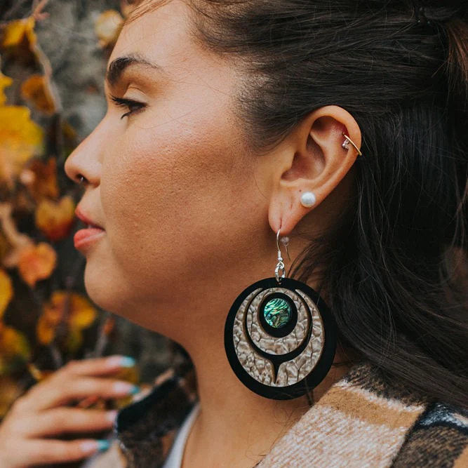 The "Owl Eye" earring in desert pattern acrylic from Copper Canoe Woman worn by a model standing in profile.