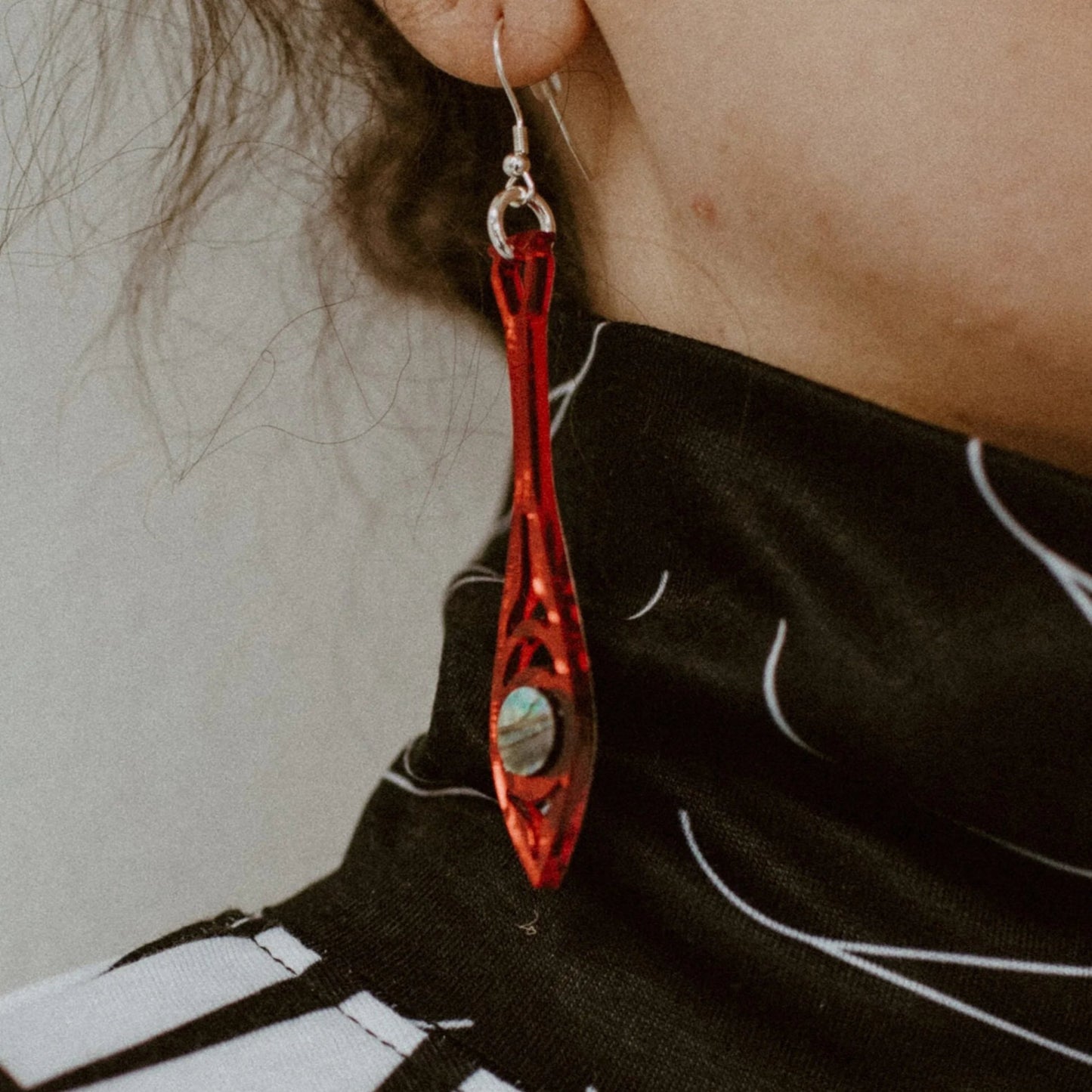 Closeup of a red mirror acrylic "Paddle Song" earring from Copper Canoe Woman worn by a model.