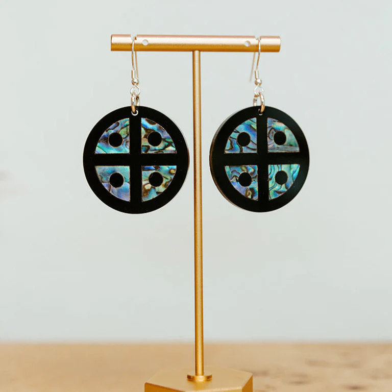 Copper Canoe Woman "Protector Shield" earrings in black acrylic with abalone inlay hang from an earring stand.