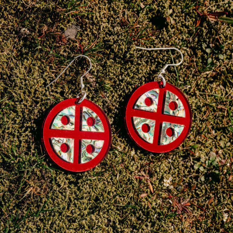 Closeup of red mirror acrylic "Protector Shield" earrings from Copper Canoe Woman on a bed of moss.