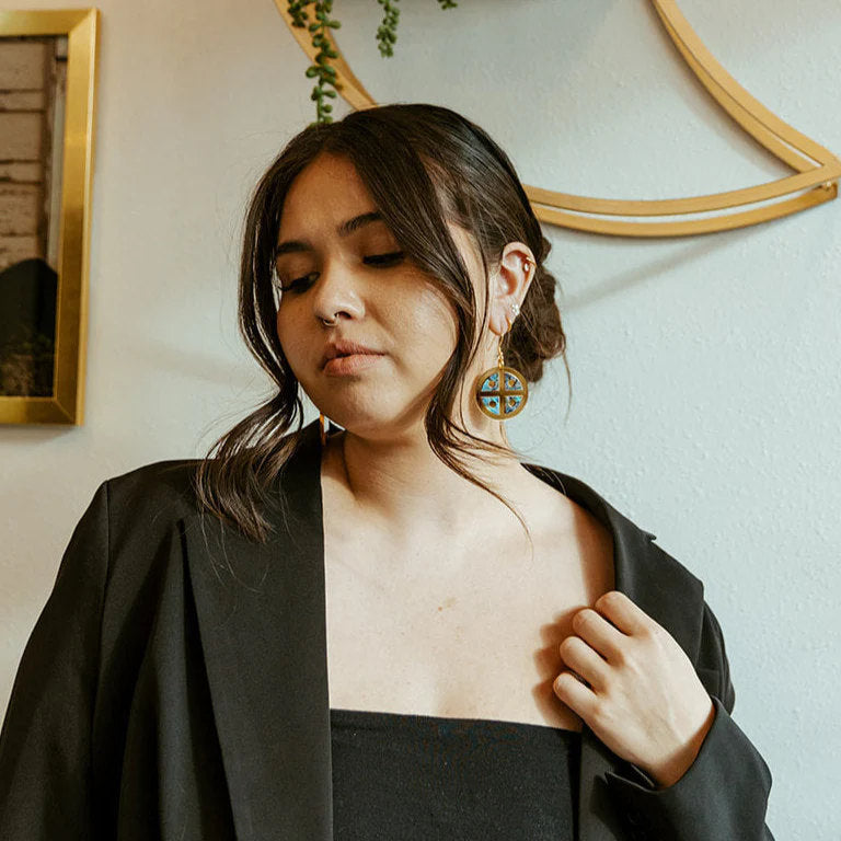 A woman wearing the gold mirror acrylic "Protector Shield" earring from Copper Canoe Woman.