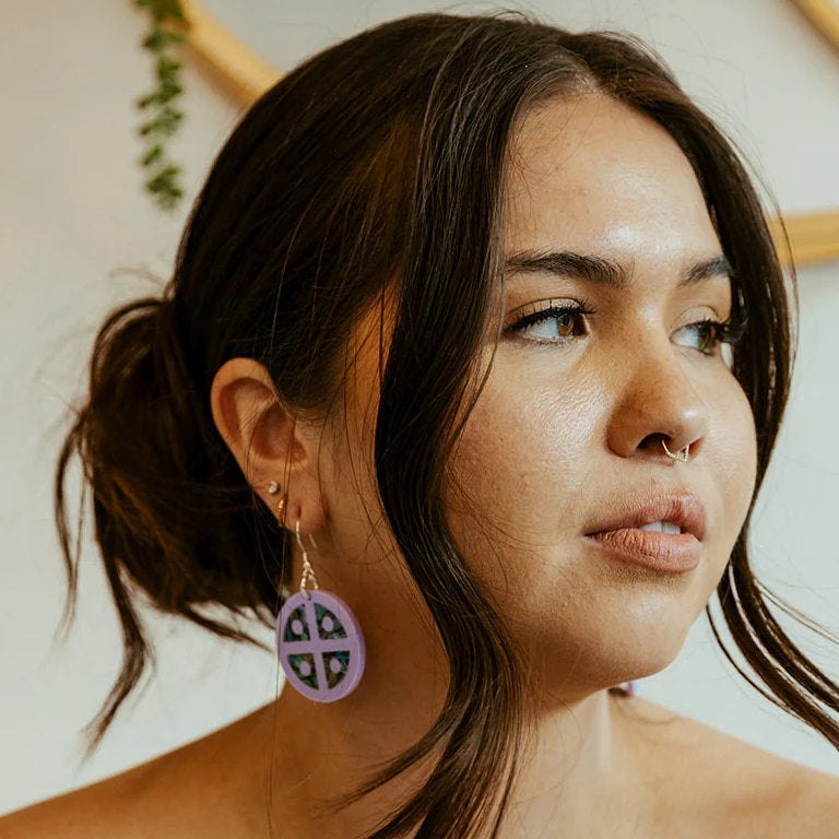 Profile of a model wearing "Protector Shield" earrings from Copper Canoe Woman in lavender acrylic.