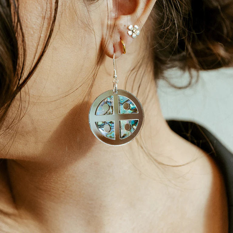 A closeup of a model wearing Copper Canoe Woman "Protector Shield" earrings in silver mirror acrylic.
