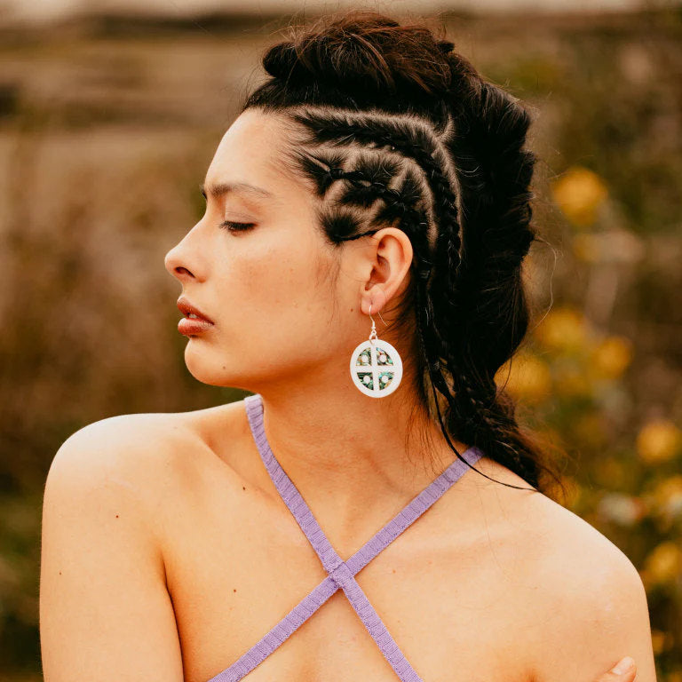 Copper Canoe Woman "Protector Shield" earrings in white acrylic with abalone inlay worn by a model in a field.