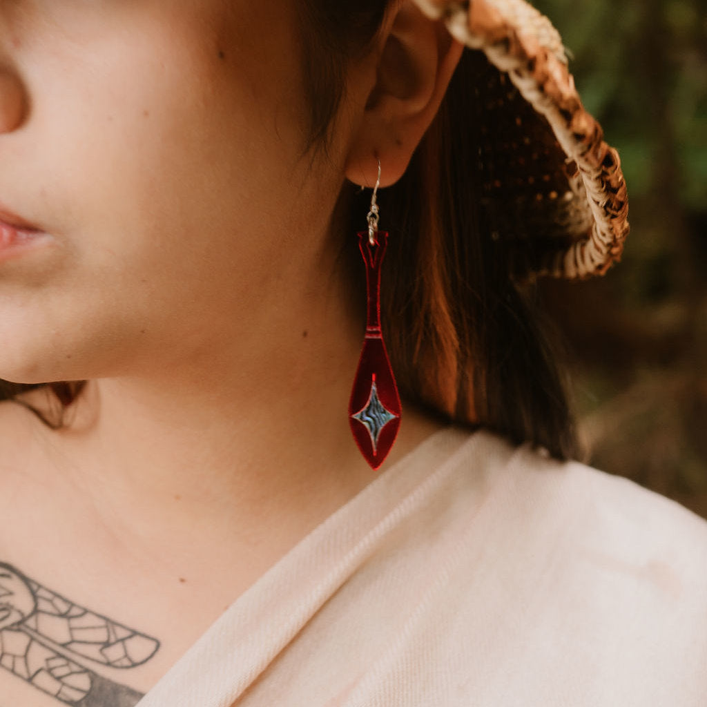 Close-up of a person wearing a red mirror acrylic paddle shaped earring from Copper Canoe Woman with star shaped abalone inlay.